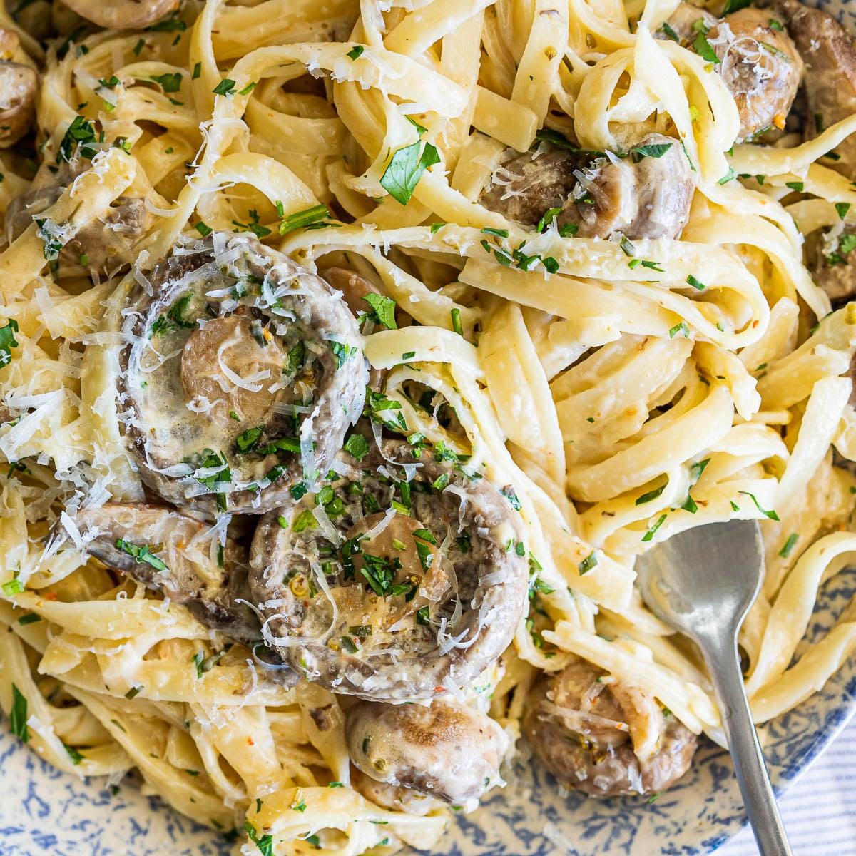 Creamy lemon garlic mushroom pasta in a white bowl, garnished with fresh parsley and grated Parmesan cheese, showing golden seared mushrooms in rich cream sauce