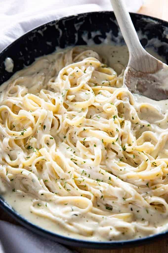 Creamy homemade alfredo sauce being whisked in a pan with fresh parmesan and garlic