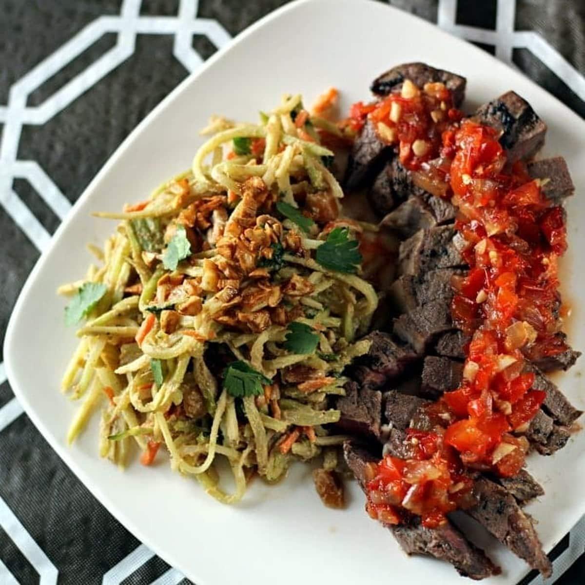Crying Tiger Steak (Suea Rong Hai) with caramelized edges, sliced against the grain and served with Thai relish on a wooden cutting board