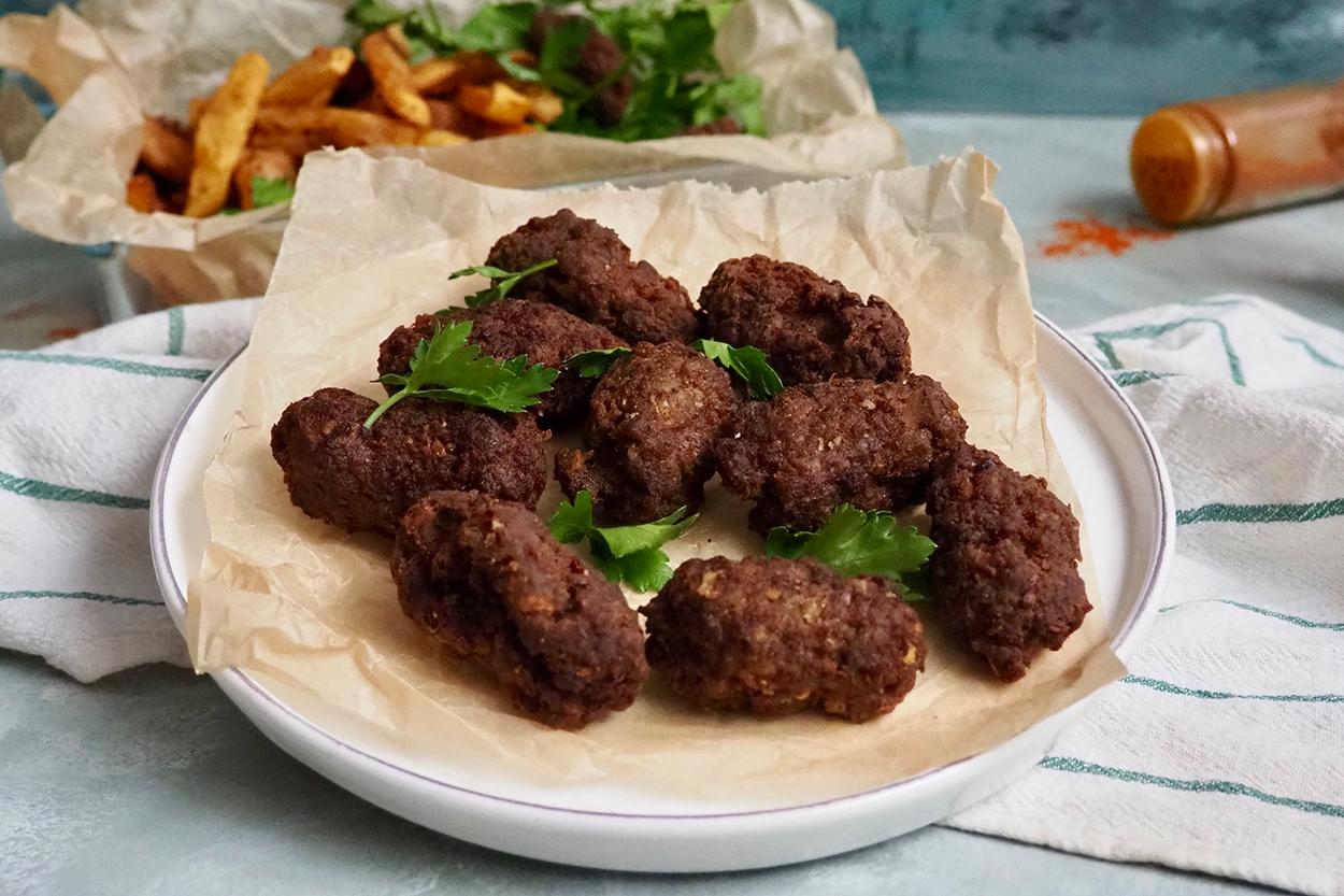 Golden brown Turkish kuru köfte meatballs on a white plate with fresh herbs and yogurt sauce