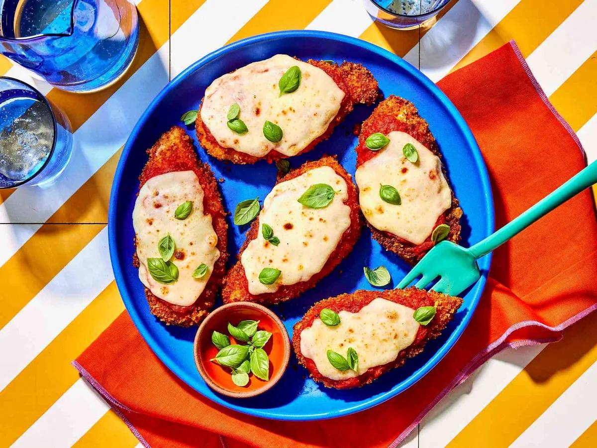 Golden crispy chicken parmesan with melted cheese and marinara sauce on a white plate, garnished with fresh basil