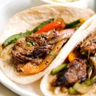 Sizzling steak fajitas with perfectly charred marinated beef strips, colorful bell peppers and onions in a cast iron skillet