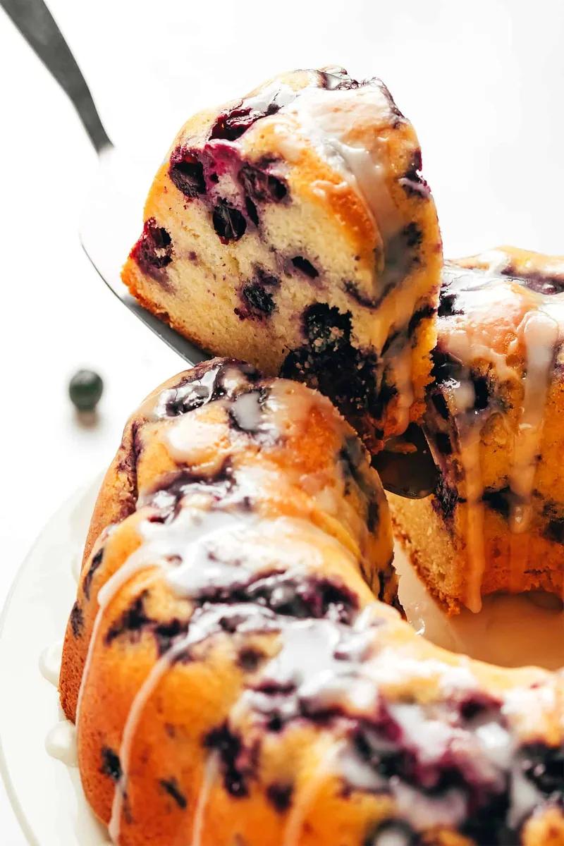 Golden blueberry bundt cake with white glaze dripping down sides, fresh blueberries scattered around