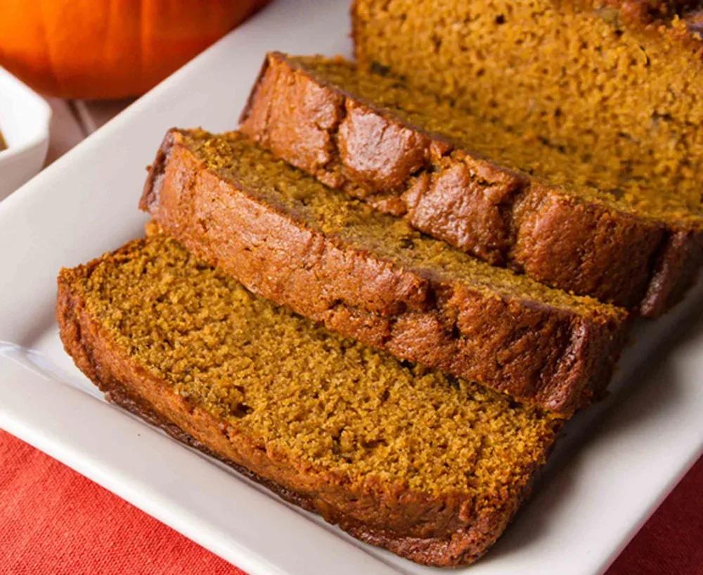 A sliced loaf of pumpkin bread with a golden, domed top and a moist, orange-brown crumb on a wooden board
