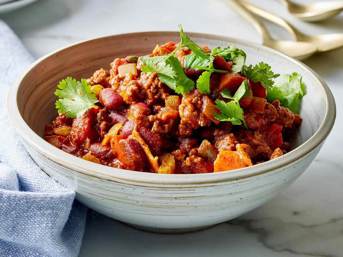 Bowl of award-winning chili topped with cheese and green onions, surrounded by cornbread and toppings