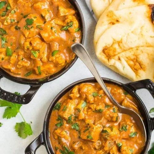 Creamy slow cooker butter chicken with tender cauliflower in rich tomato sauce served over rice with fresh cilantro garnish