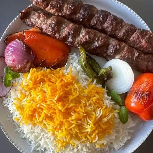 Juicy Persian kabob koobideh grilling over hot coals with char marks and smoky flames