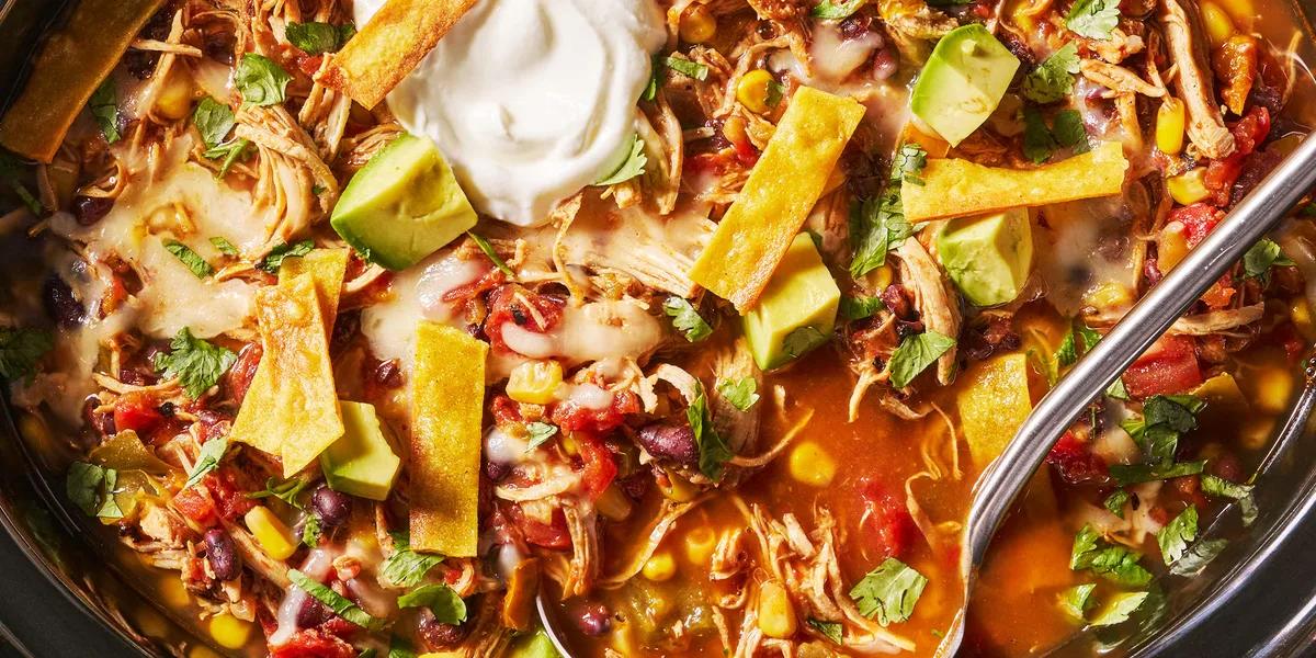 Bowl of slow cooker chicken tortilla soup topped with golden tortilla crisps, diced avocado, sour cream, and fresh cilantro