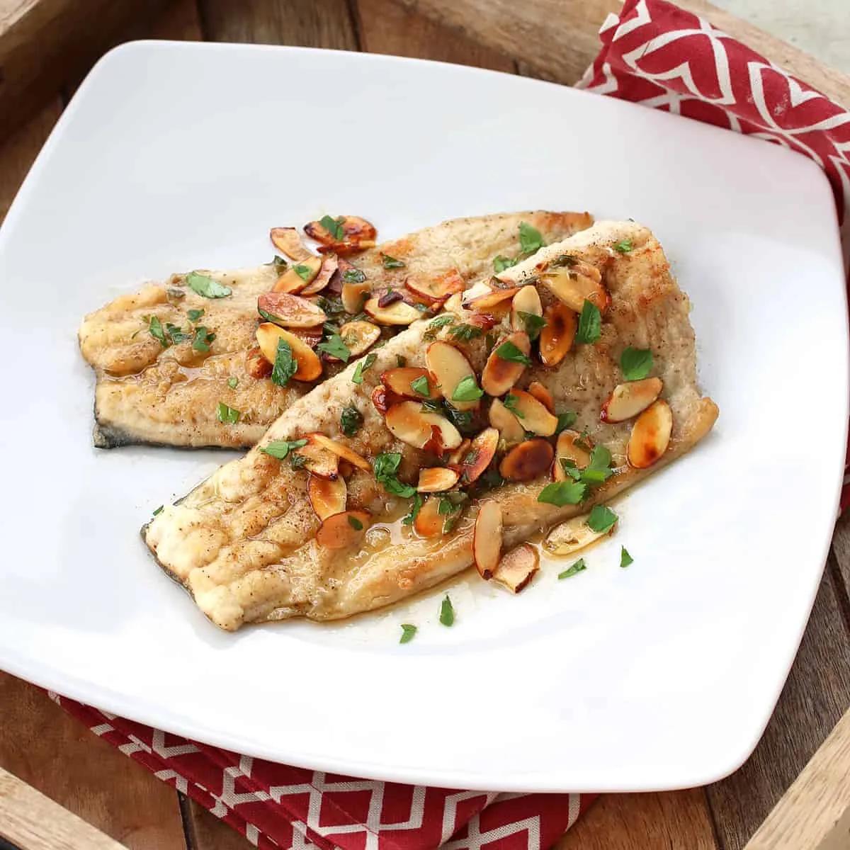Golden pan-fried trout almondine with toasted almonds and fresh parsley in lemon butter sauce on white plate