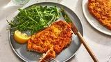 Golden crispy Chicken Milanese cutlets on white plate with fresh arugula salad and lemon wedges, Italian comfort food