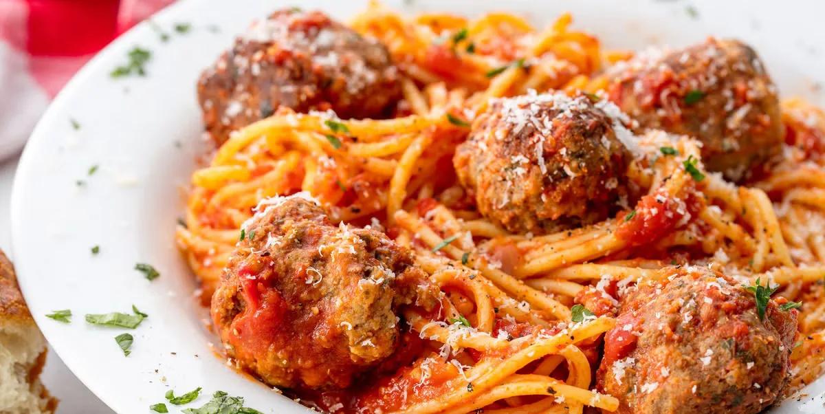 Homemade spaghetti and meatballs with rich tomato sauce and fresh Parmesan cheese on white plate