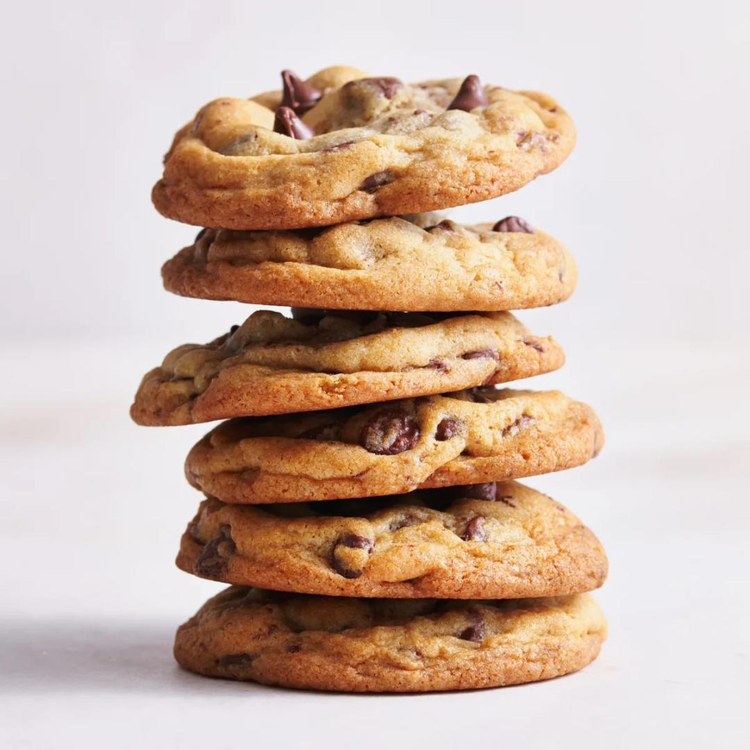 A stack of thick bakery style chocolate chip cookies with golden edges and melted chocolate pools on a cooling rack