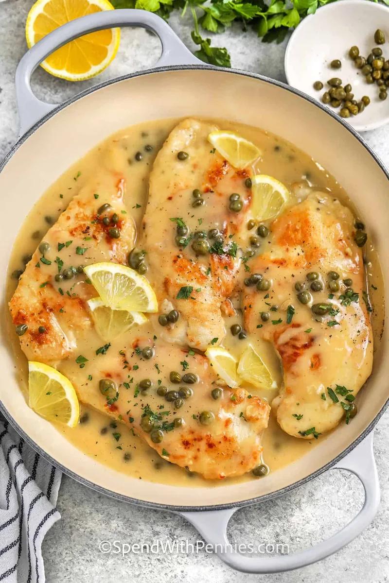 Golden chicken piccata in creamy lemon caper sauce garnished with fresh parsley in a stainless steel skillet
