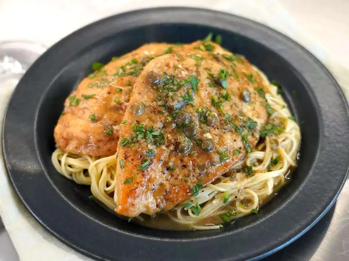 Golden chicken piccata in a skillet with bright lemon caper sauce and fresh parsley garnish
