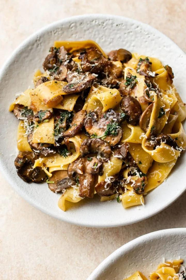 Creamy garlic mushroom pasta with golden caramelized mushrooms, fresh parsley, and grated parmesan cheese in a white bowl