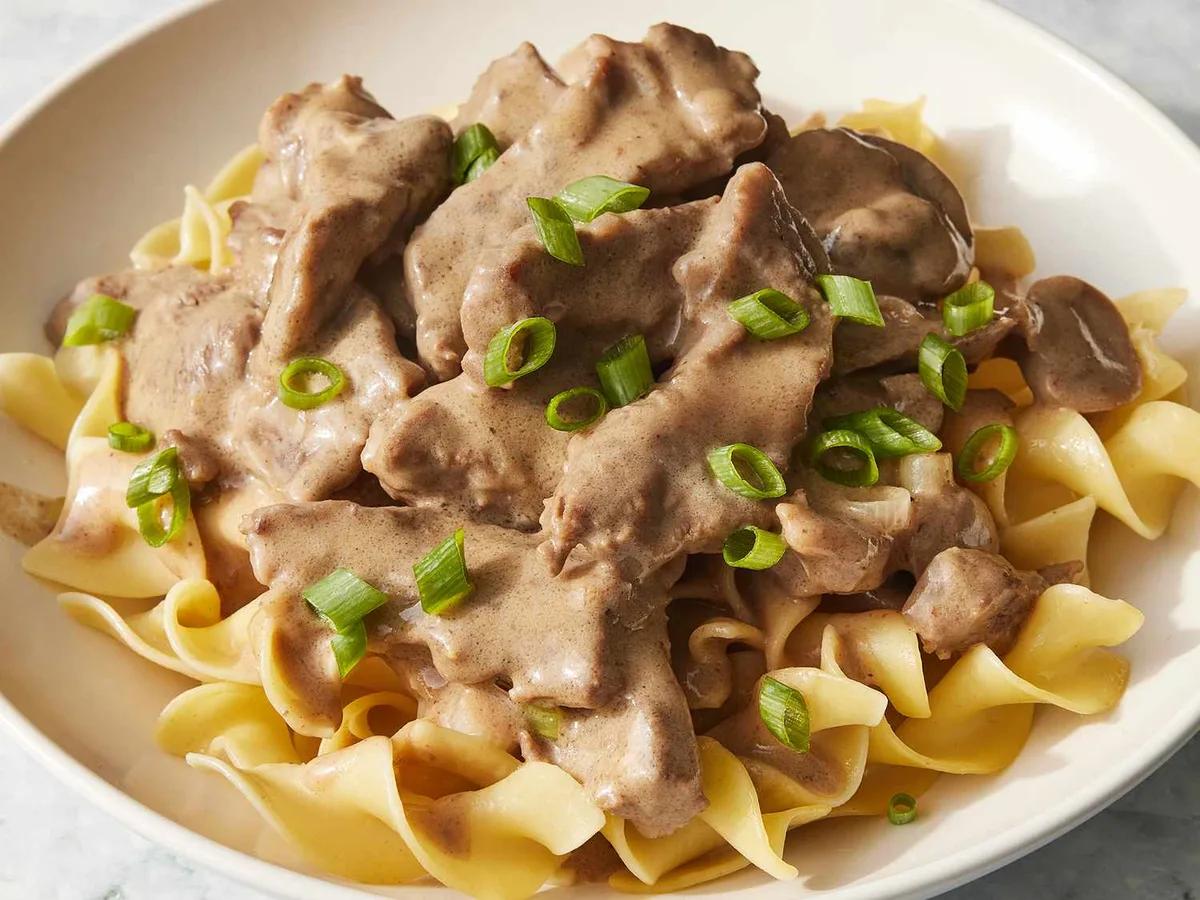 Creamy beef stroganoff with tender chuck roast and mushrooms served over egg noodles in a white bowl