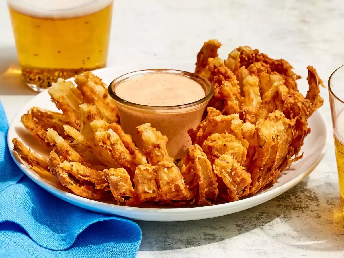 Golden brown blooming onion with crispy petals spread open like a flower, served with creamy horseradish dipping sauce
