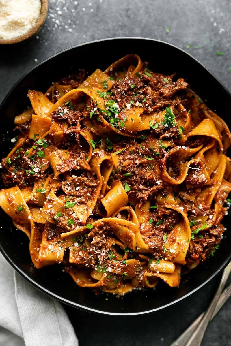 Slowly braised short rib ragu with tender shredded beef in rich tomato sauce served over pappardelle pasta with parmesan cheese