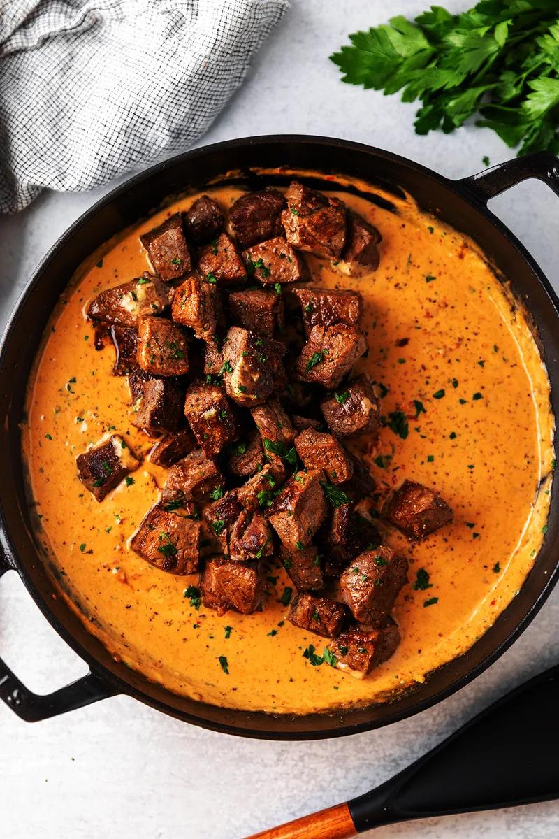 Creamy Tuscan marry me steak bites in rich sun-dried tomato cream sauce served over mashed potatoes