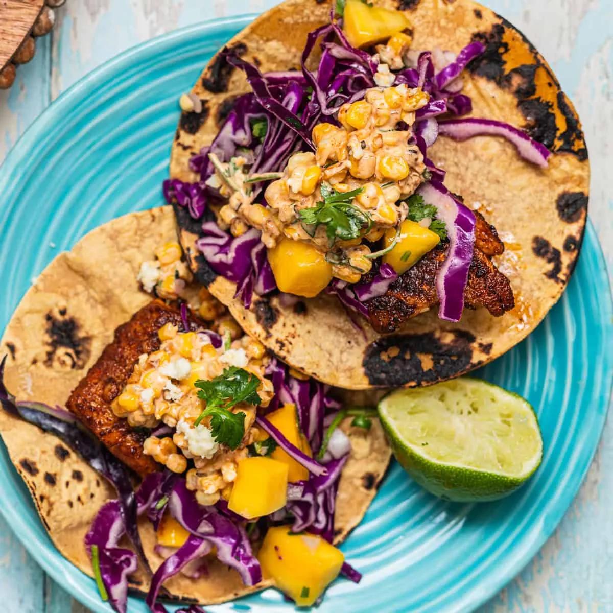 Spicy blackened fish tacos topped with mango slaw and elote salad on corn tortillas