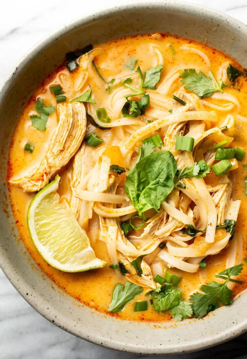 Thai chicken curry soup with rice noodles, basil and cilantro in a bowl