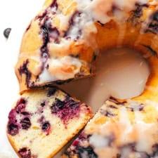 Golden blueberry bundt cake with white glaze dripping down sides, fresh blueberries scattered around
