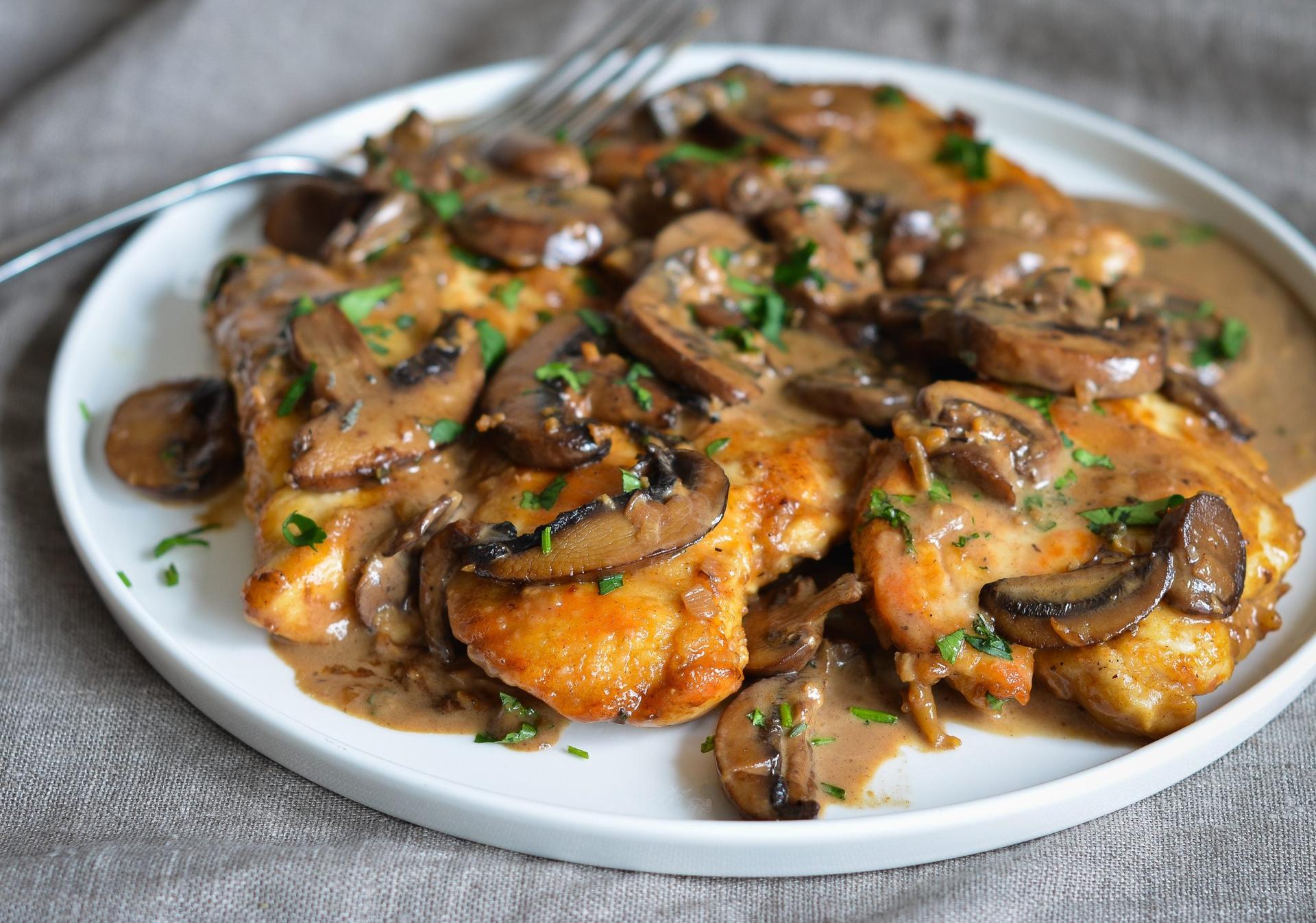 Golden chicken marsala with mushrooms in rich wine sauce served on white plate with fresh herbs