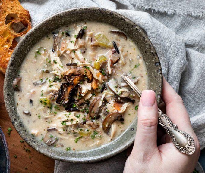 Creamy chicken wild rice soup in a white bowl topped with golden mushrooms and fresh herbs